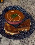 Roasted red pepper soup with a grilled cheese sandwich on a patterned plate.