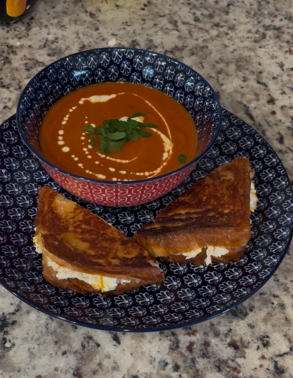 Roasted red pepper soup with a grilled cheese sandwich on a patterned plate.